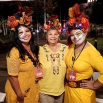 Three women in matching yellow outfits and flower crowns wearing festival VIP badges